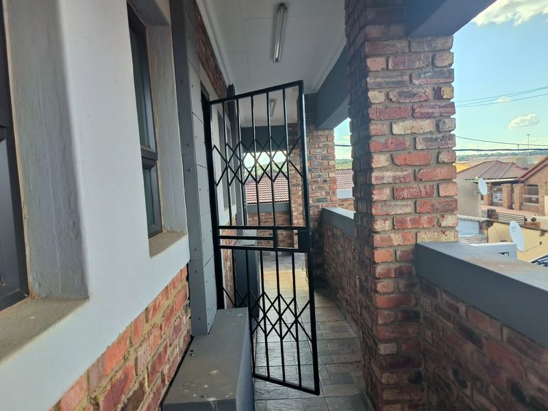 A covered balcony featuring exposed brick pillars, tiled flooring, and a secure metal gate, offering an outdoor space with neighbourhood views.