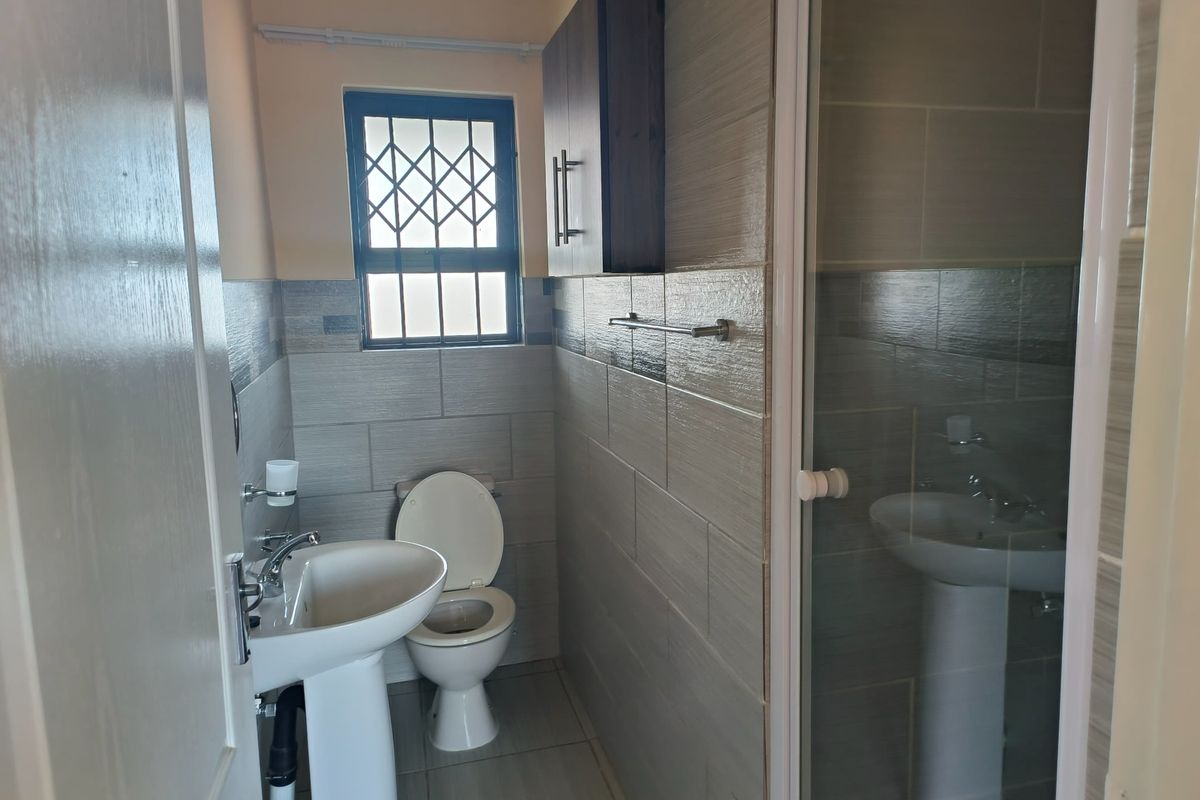 A clean, modern bathroom featuring a pedestal basin, toilet, and a glass-enclosed shower with neutral wall and floor tiling.