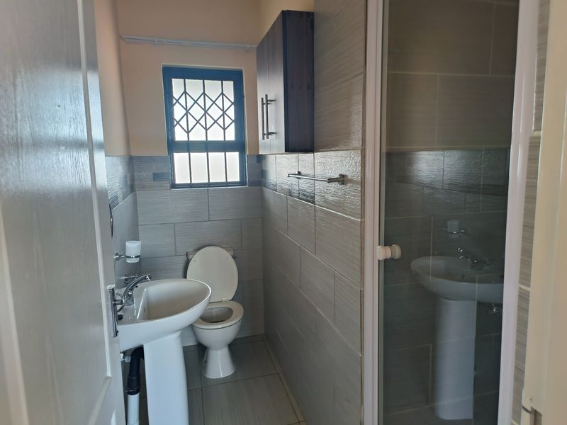 A clean, modern bathroom featuring a pedestal basin, toilet, and a glass-enclosed shower with neutral wall and floor tiling.
