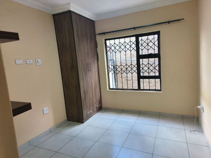 A clean, empty bedroom featuring tiled flooring, a built-in wooden wardrobe, and a window fitted with a security gate.