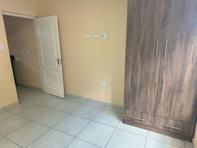 A clean, empty bedroom featuring neutral wall paint, light-colored floor tiles, and a modern wood-finish built-in wardrobe.