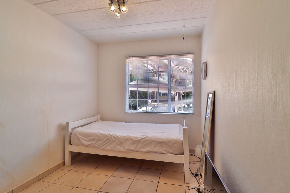 A simple bedroom featuring tiled flooring, a window with venetian blinds, and a ceiling-mounted spotlight fixture.