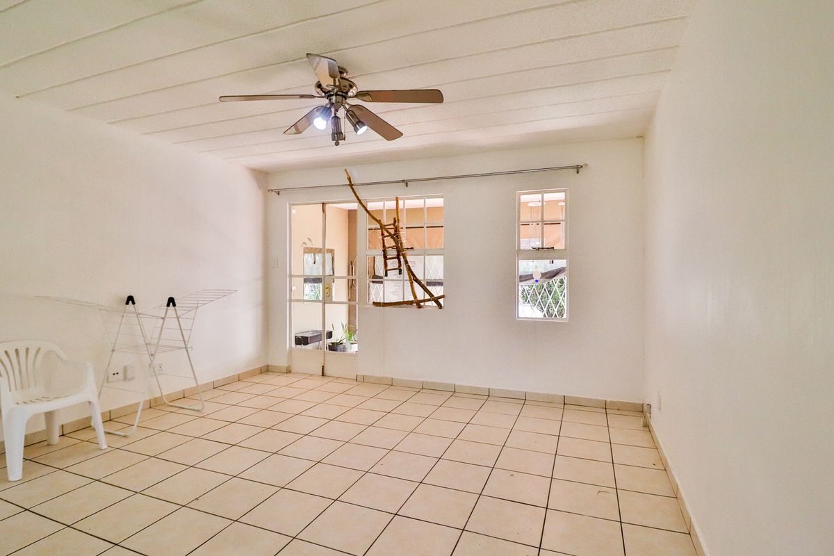 A bright, empty living area featuring neutral tiled flooring, a ceiling fan, and glass panel doors leading to an adjacent space.