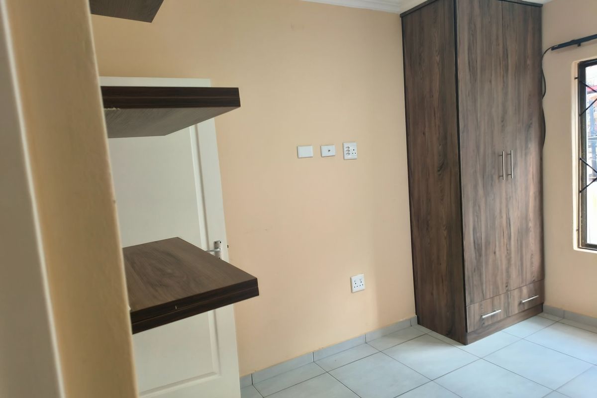 A clean, empty bedroom featuring tiled flooring, a built-in wooden wardrobe, and wall-mounted floating shelves.