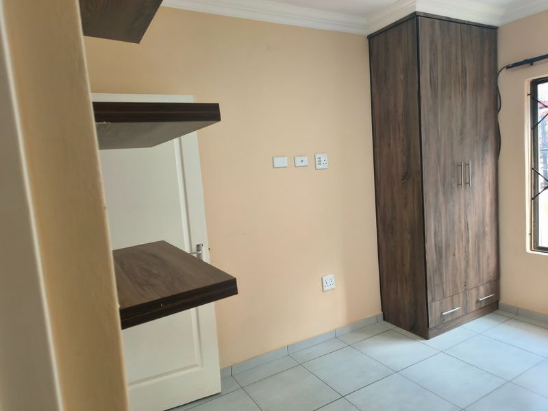 A clean, empty bedroom featuring tiled flooring, a built-in wooden wardrobe, and wall-mounted floating shelves.