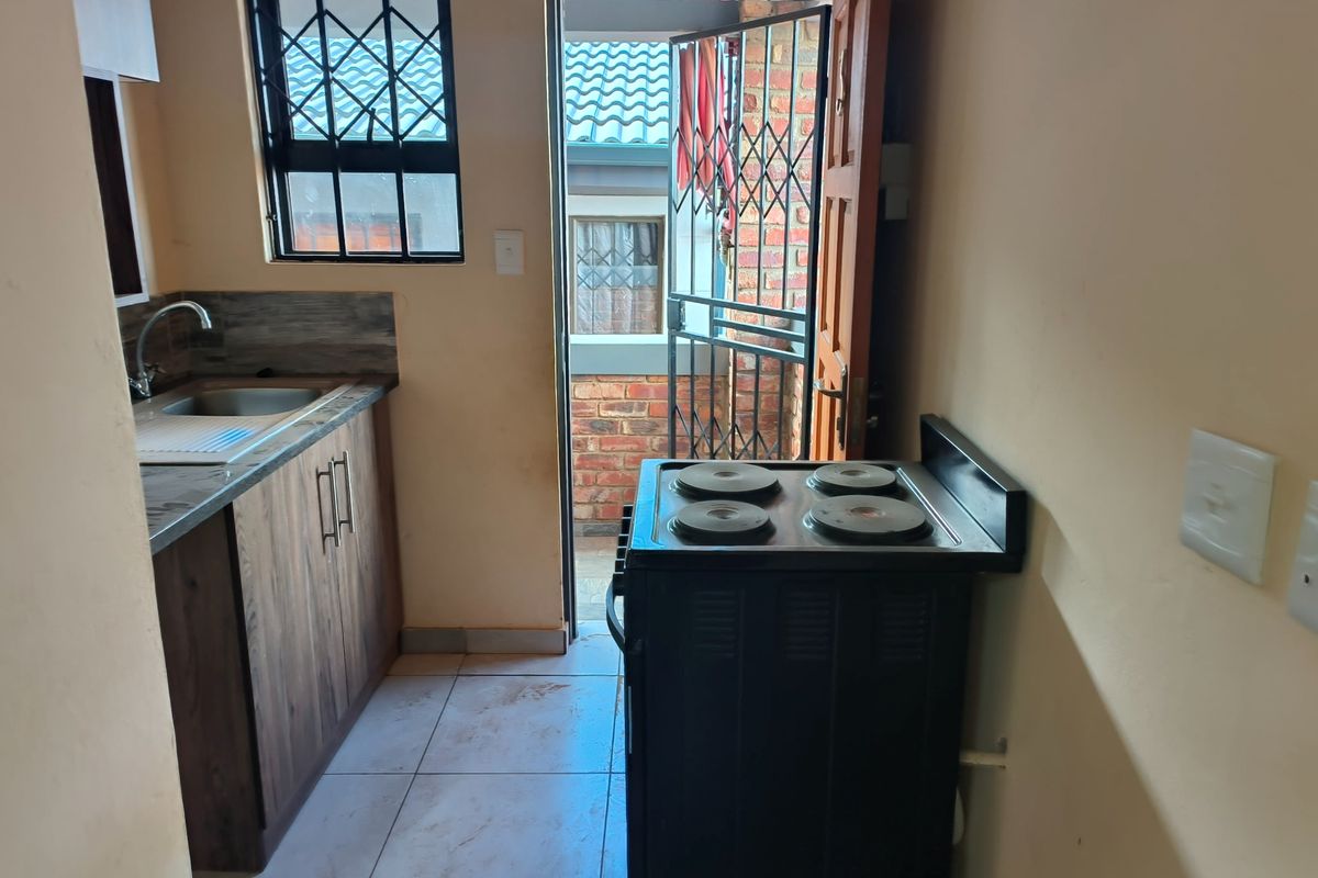 Compact kitchen featuring wood-look cabinetry, stainless steel sink, tiled flooring, and direct access to an exterior area through a security gate.