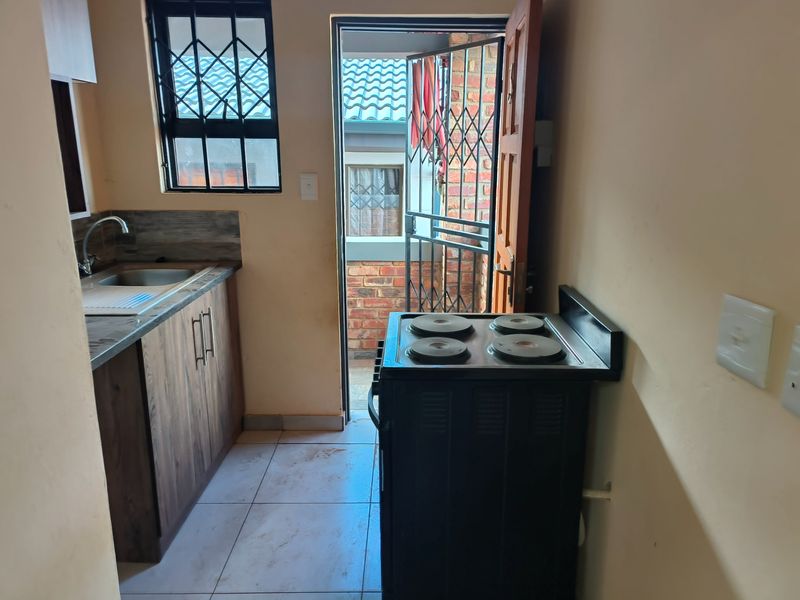 Compact kitchen featuring wood-look cabinetry, stainless steel sink, tiled flooring, and direct access to an exterior area through a security gate.