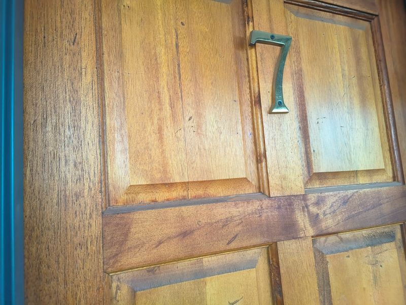 Close-up view of a solid timber front door featuring a brass house number seven.