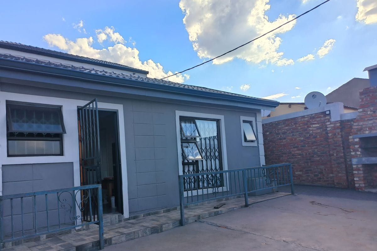Rear exterior view of the flat featuring a paved patio area, security gates, and a brick boundary wall.
