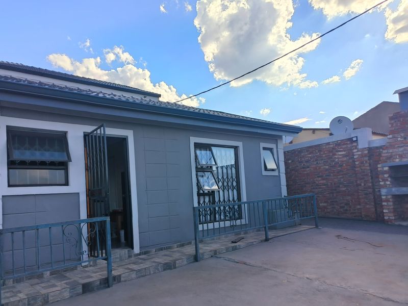 Rear exterior view of the flat featuring a paved patio area, security gates, and a brick boundary wall.