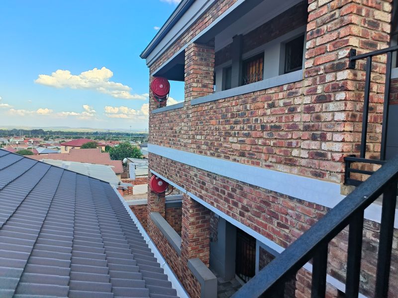 Exterior view of a multi-story face brick apartment building featuring metal railings, tiled roofing, and mounted fire hose reels.
