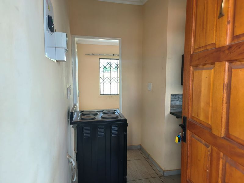 A compact kitchen area featuring tiled flooring, an electric stove, and a wooden entrance door leading to an adjacent room with security bars.