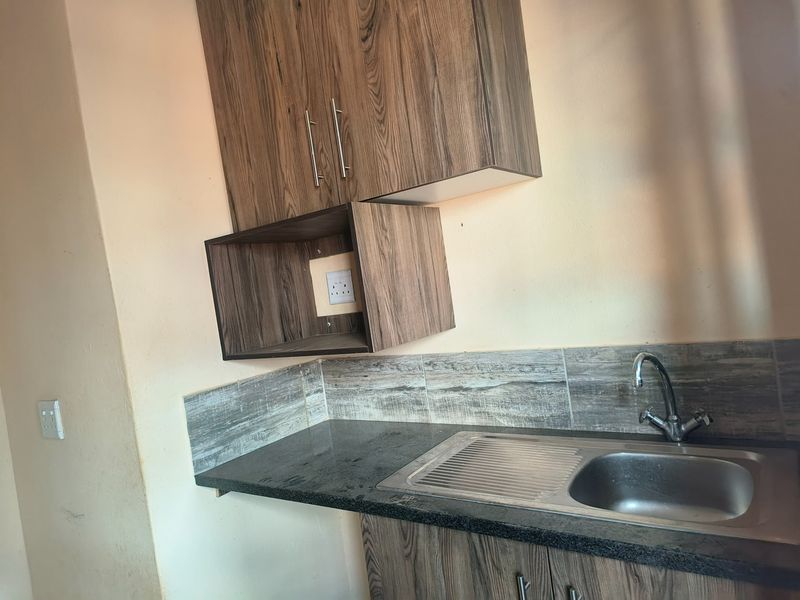 A compact kitchen area featuring wood-look cabinetry, granite countertops, and a stainless steel sink with a tiled splashback.