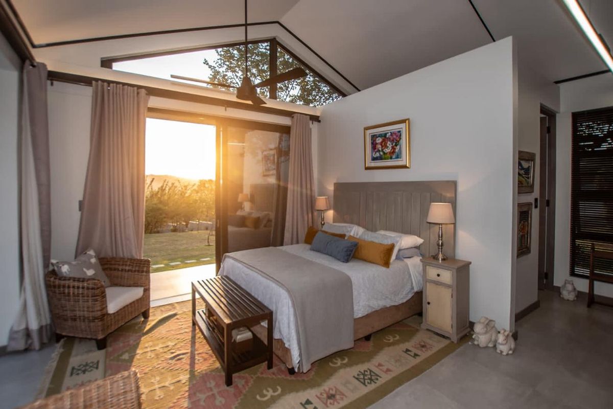 A bright bedroom featuring a vaulted ceiling, ceiling fan, and large sliding glass doors that open to an outdoor view.