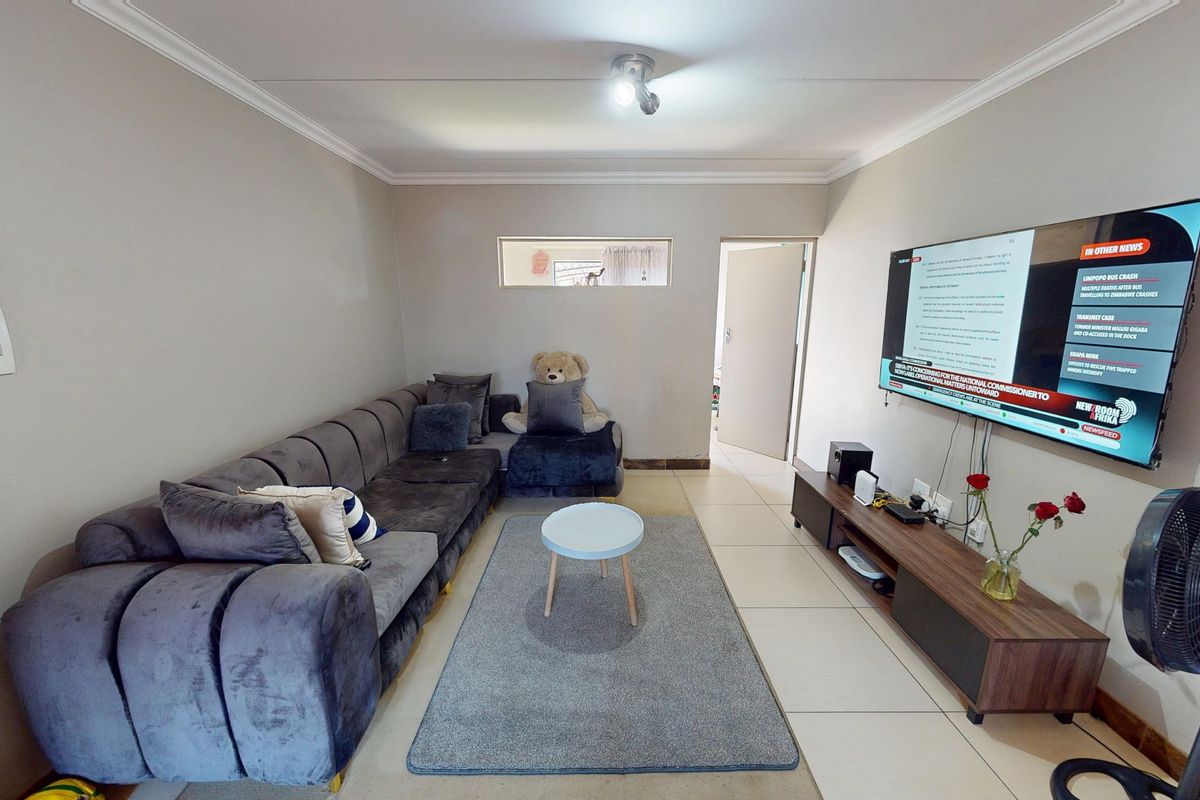 A well-maintained living room featuring tiled flooring, cove cornicing, and a wall-mounted television setup.