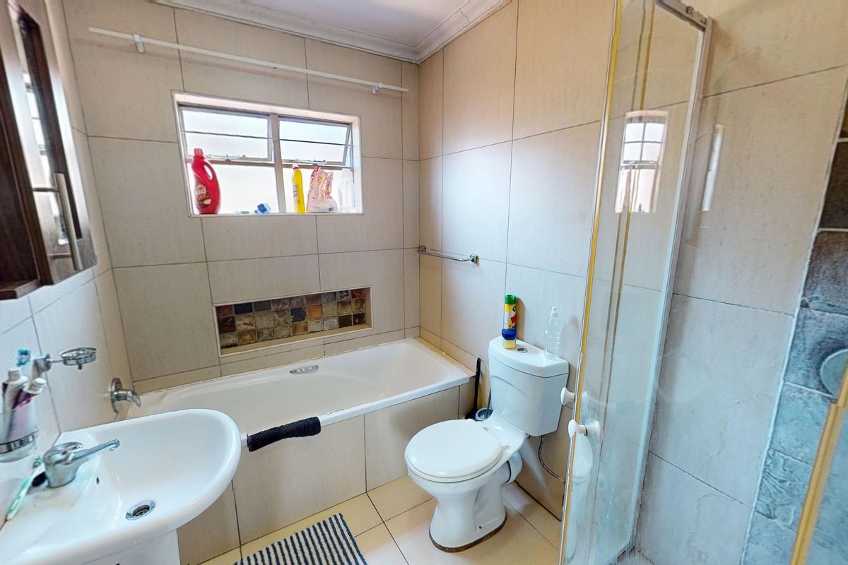 A functional bathroom featuring a bathtub, separate shower enclosure, pedestal basin, and toilet, finished with neutral wall and floor tiling.