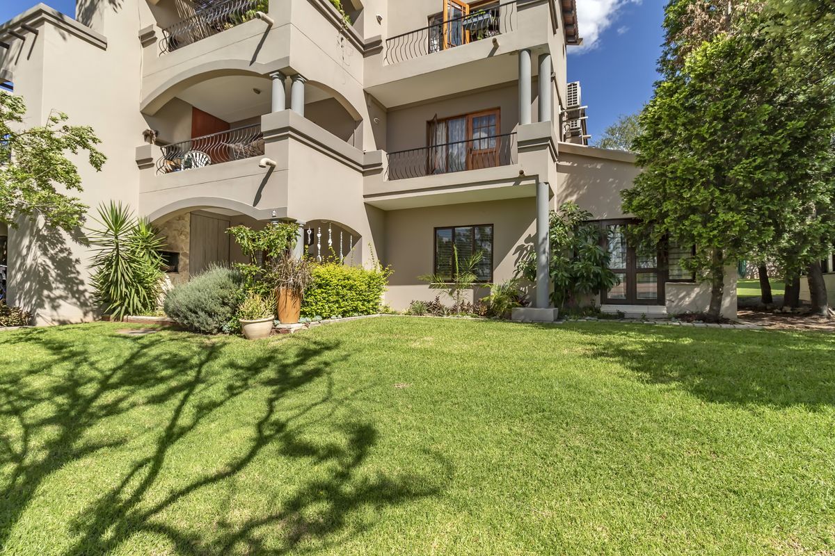 Exterior view of a multi-story apartment building featuring private balconies with wrought iron railings and a well-maintained ground-level garden area.
