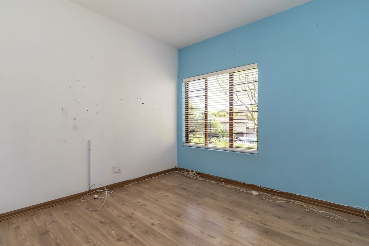 An empty bedroom featuring wood-look laminate flooring, a blue accent wall, and a window fitted with horizontal blinds.