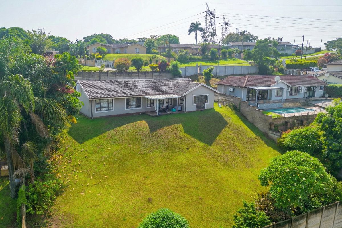 Aerial view of a residential property featuring a tiled roof house, a spacious lawn, and a concrete boundary wall in a suburban setting.
