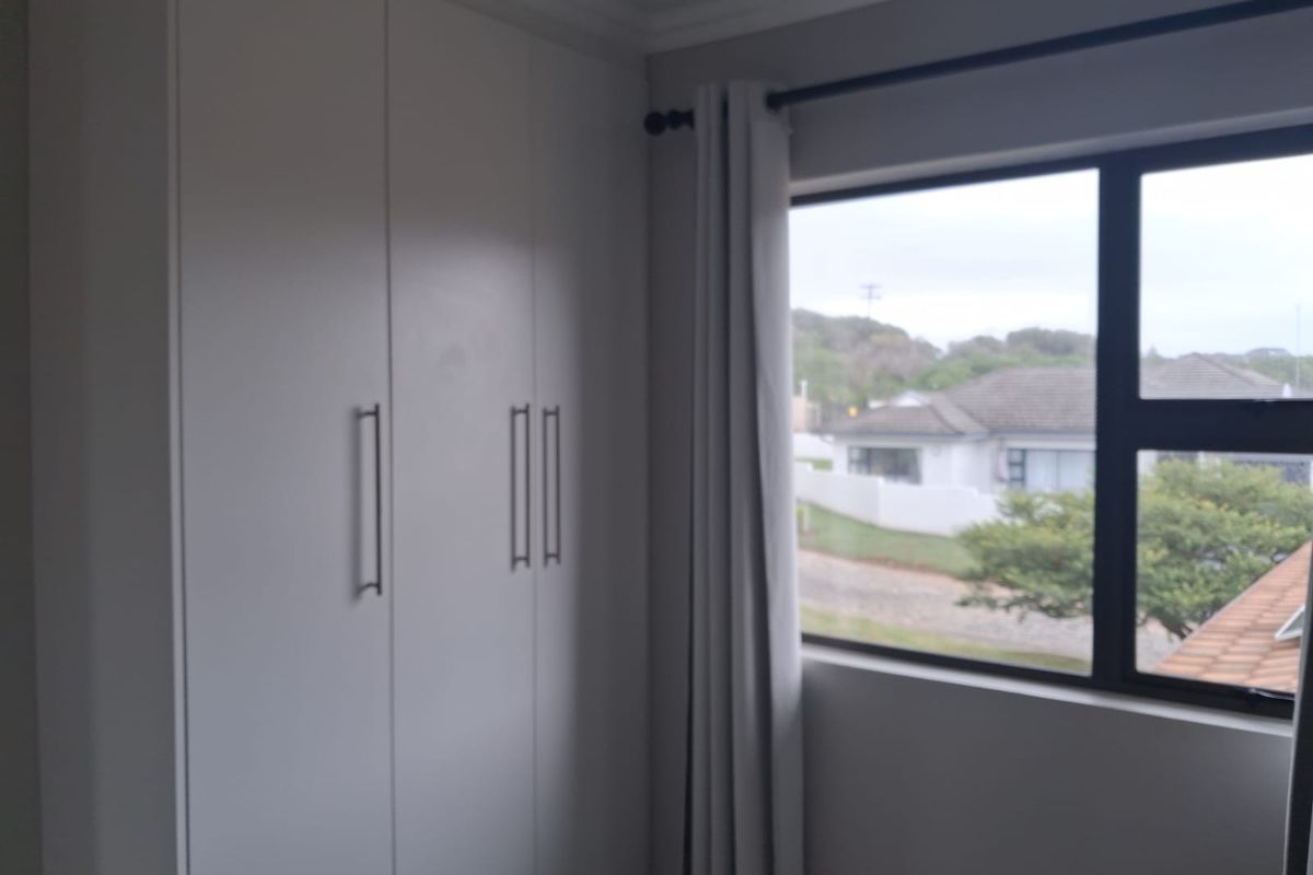 A bedroom featuring built-in cupboards with modern handles and a window providing natural light and a view of the surrounding neighborhood.