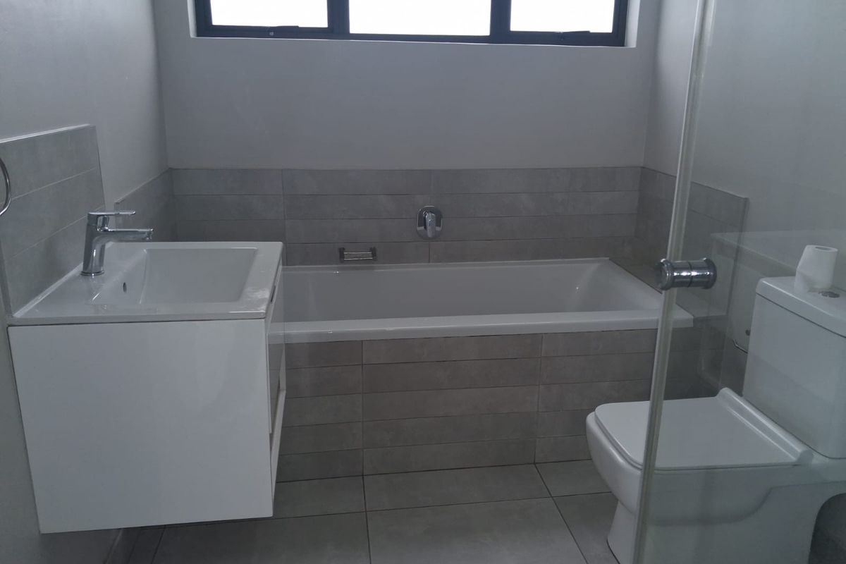 Modern bathroom featuring a wall-mounted vanity, a built-in bathtub with tiled surround, and a glass-enclosed shower area.