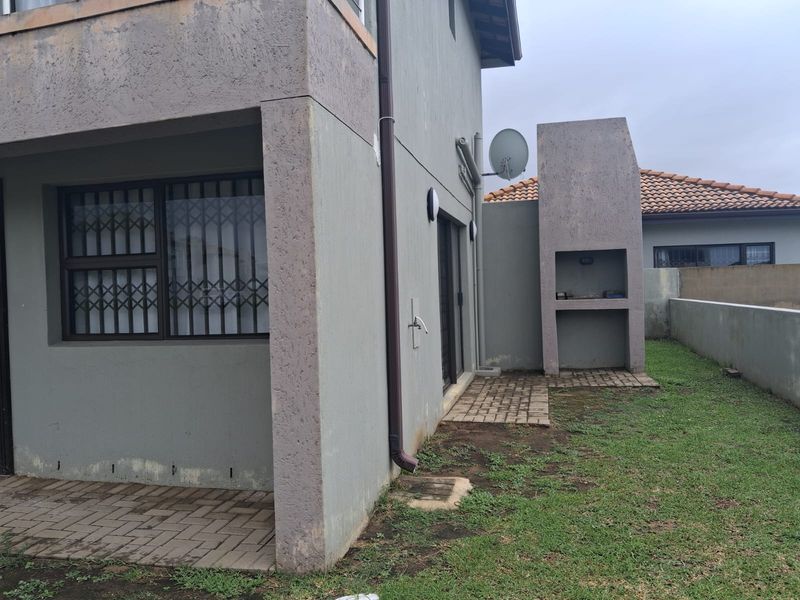Rear exterior view featuring a paved patio area, built-in braai, and a small garden space with security gates on the windows.