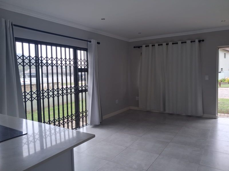 Spacious open-plan living area featuring neutral tiled flooring, recessed lighting, and direct access to the exterior through a secure sliding gate.