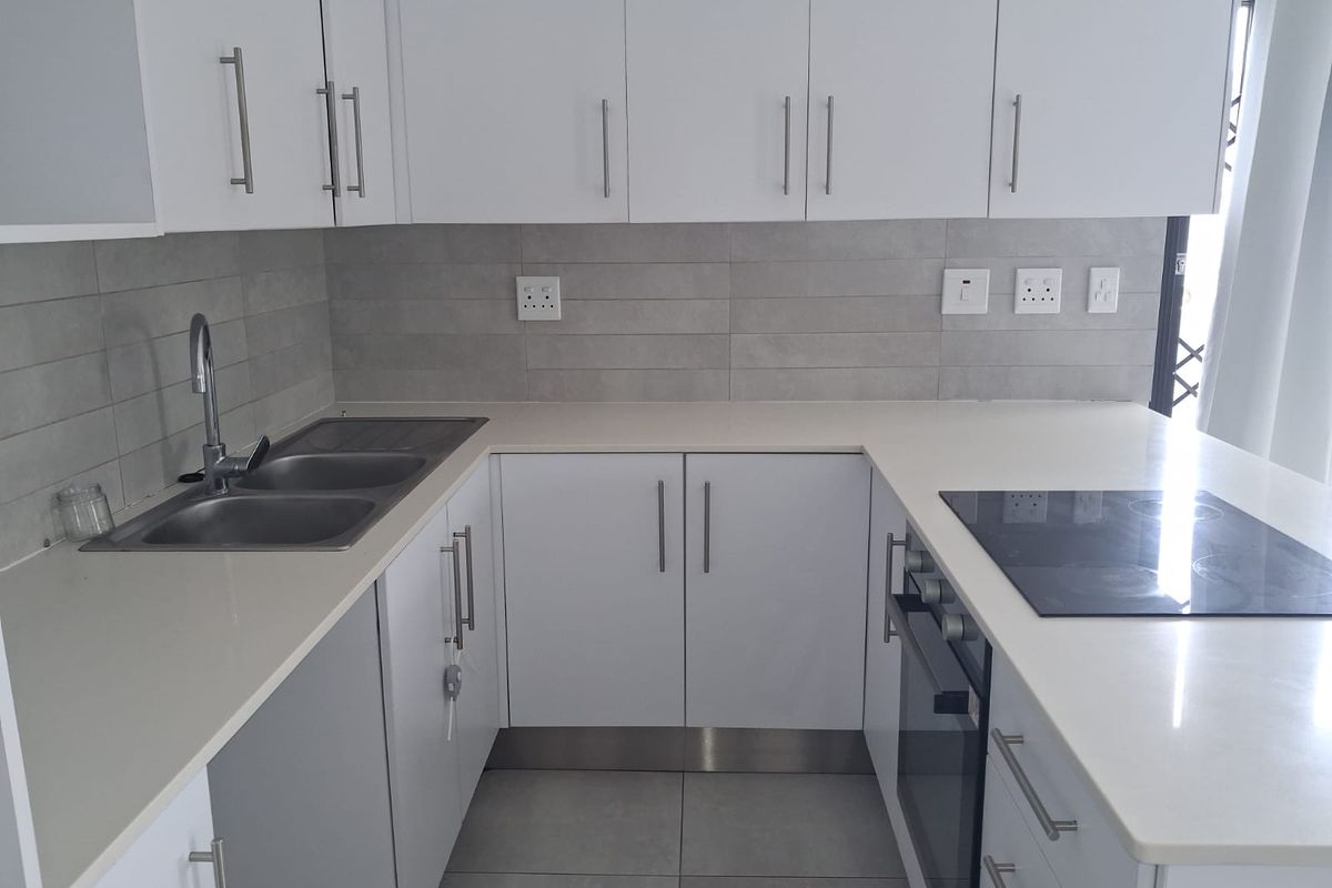 Modern kitchen featuring white cabinetry, stone countertops, integrated electric oven and hob, and a stainless steel double sink with tiled backsplash.