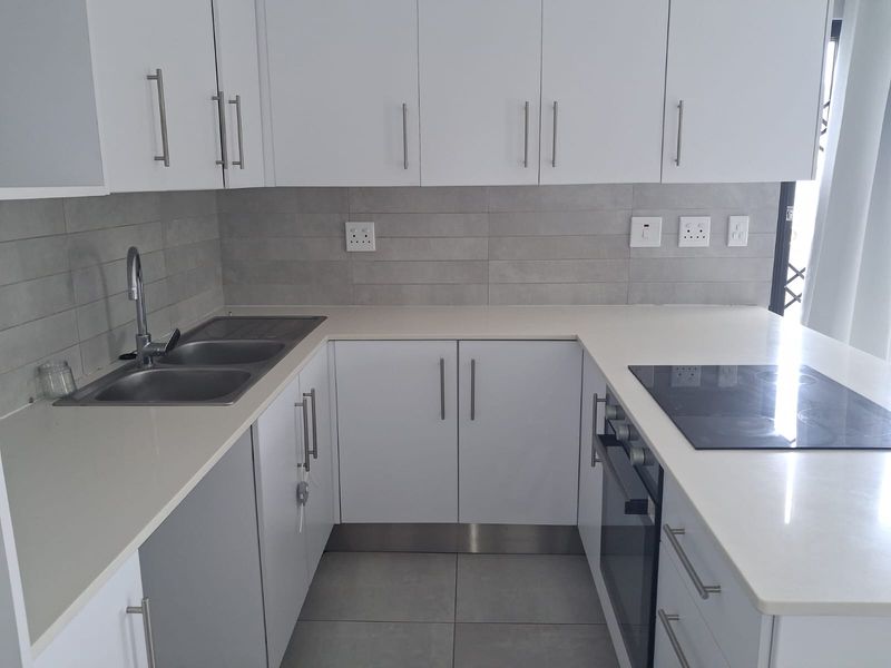 Modern kitchen featuring white cabinetry, stone countertops, integrated electric oven and hob, and a stainless steel double sink with tiled backsplash.