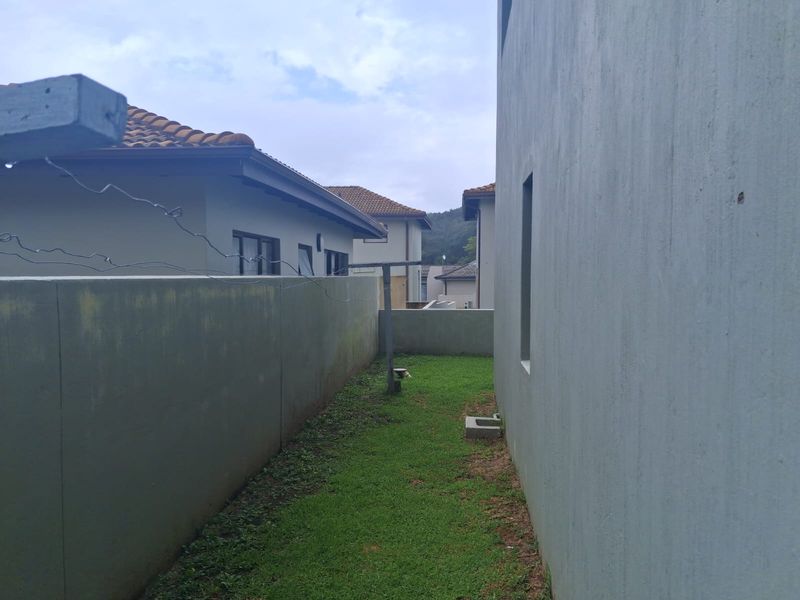 A narrow side yard area featuring a boundary wall, grass lawn, and a fixed washing line.