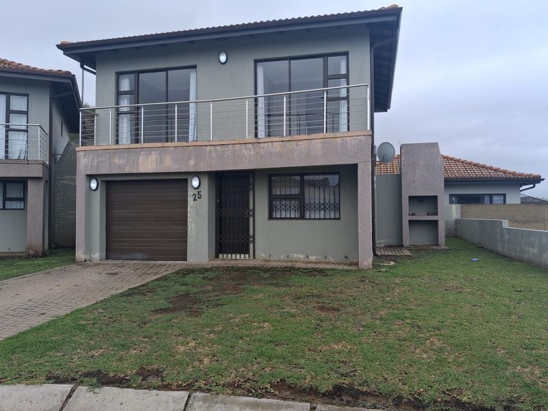 Two-story residential property featuring a garage, upper-level balcony with stainless steel railing, and an outdoor built-in braai area.