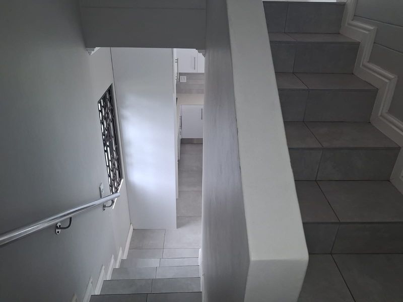 A clean, modern hallway featuring a tiled staircase with a metal handrail and neutral wall finishes.