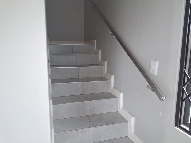 A clean, modern staircase featuring grey tiled steps and a sleek stainless steel handrail, providing a contemporary transition between levels.