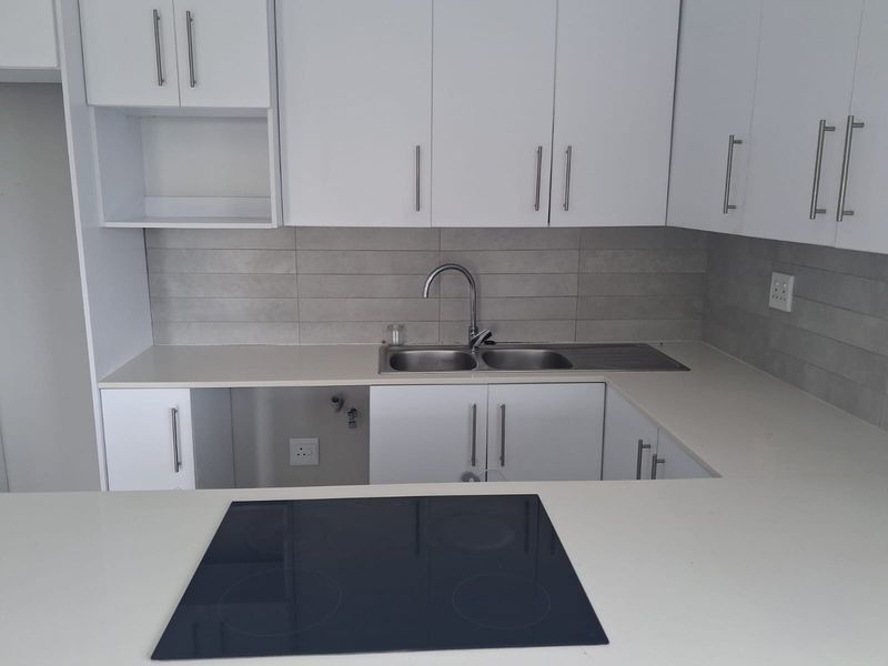 Modern kitchen featuring white cabinetry, quartz countertops, a double bowl sink, and a built-in electric induction hob with a neutral tiled backsplash.