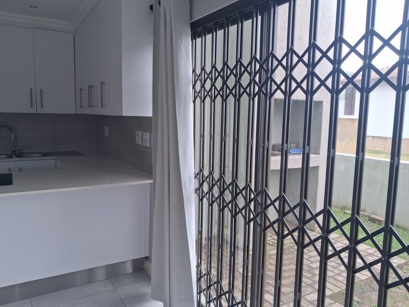 Open plan kitchen area featuring modern white cabinetry and stone countertops, with direct access through a security gate to an outdoor patio with built-in braai.