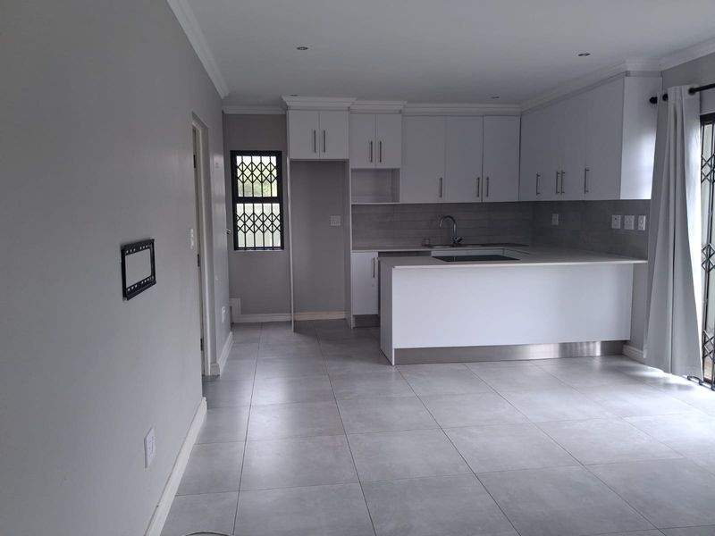 Modern open-plan kitchen featuring white cabinetry, stone countertops, integrated hob, and neutral tiled flooring, offering a clean and functional culinary space.