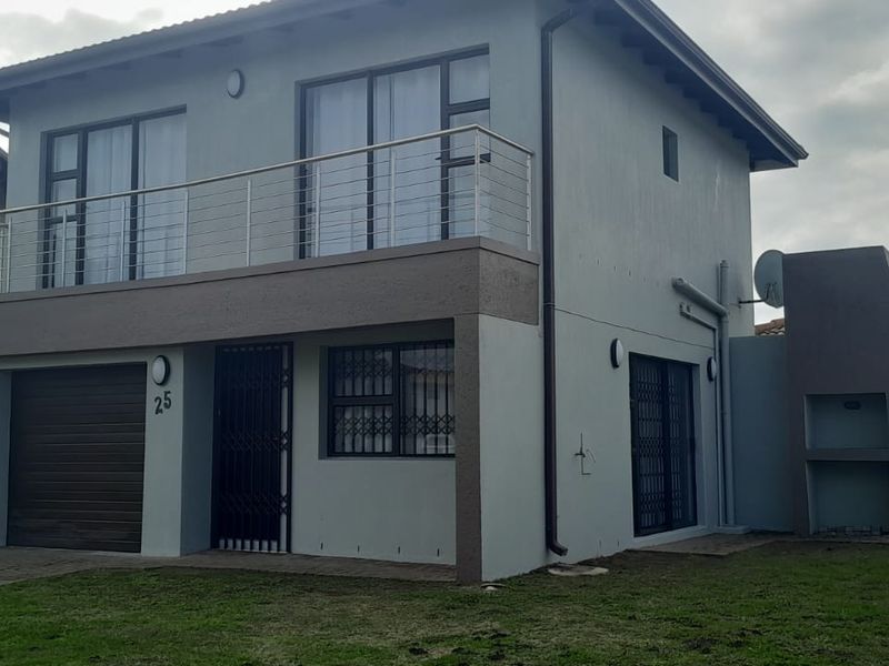 Two-story residential house featuring a balcony with stainless steel balustrade, integrated garage, and a built-in outdoor braai area.