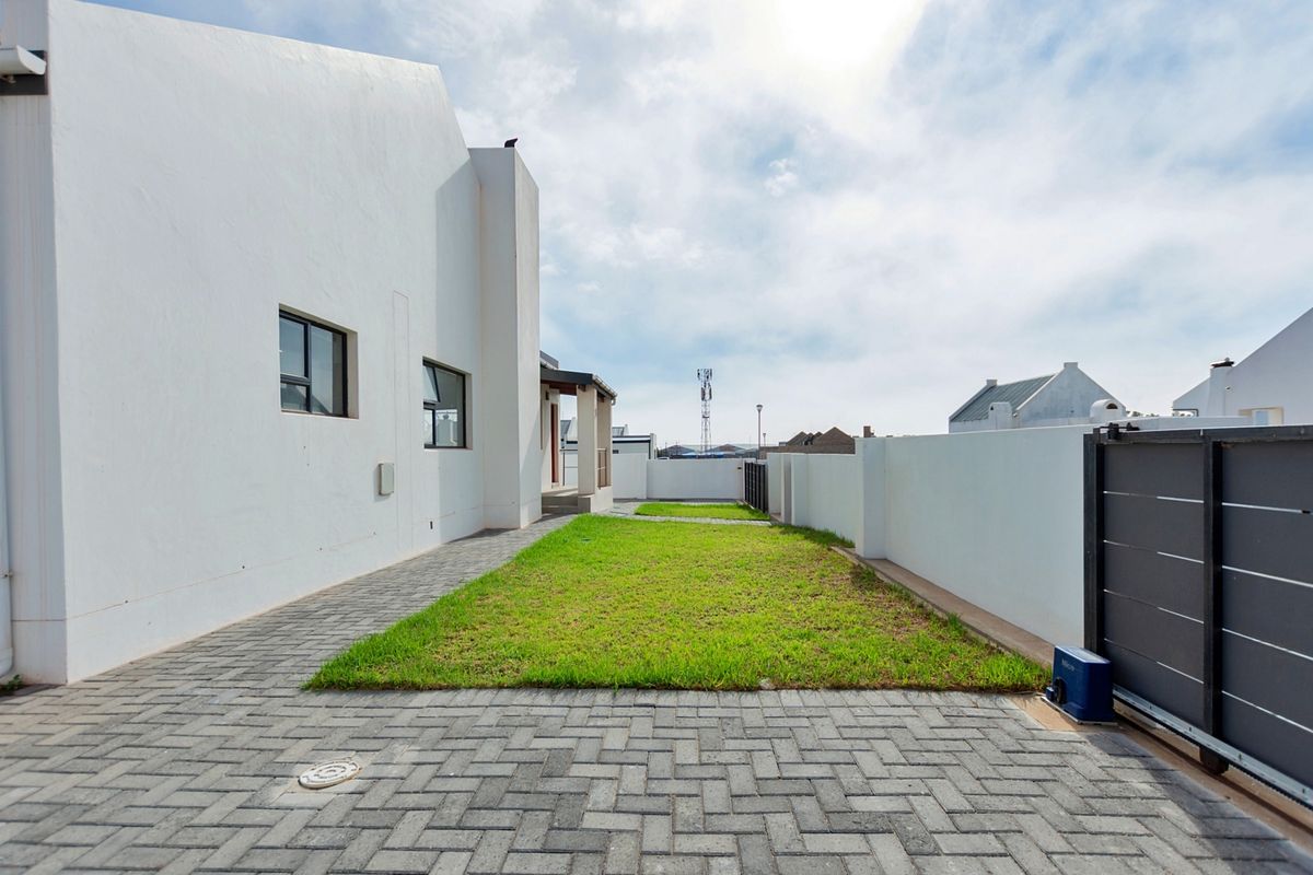 A well-maintained rear garden area featuring paved walkways, a manicured lawn, and secure perimeter walling.