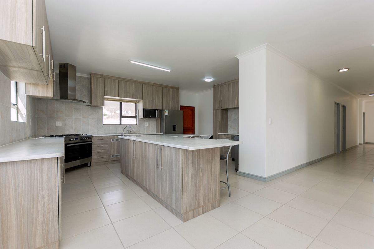 Modern open-plan kitchen featuring light wood-grain cabinetry, a central island with stone countertops, stainless steel extractor fan, and tiled flooring throughout.
