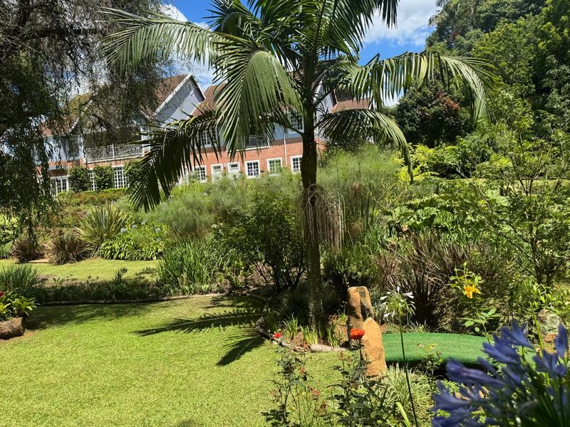A view of the rear garden and landscaped grounds featuring a lush lawn, mature trees, and the rear facade of the multi-story brick house.