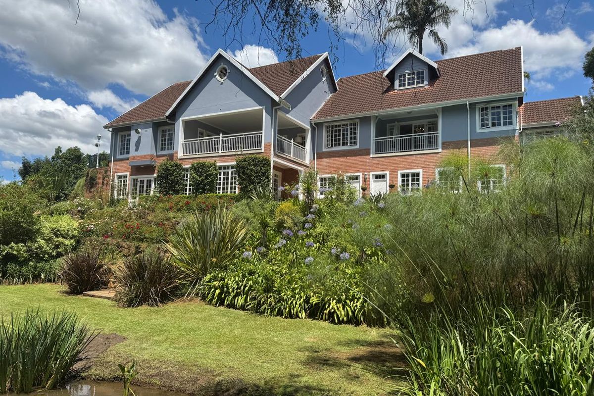 A spacious multi-story residence featuring a brick and painted facade, multiple balconies, and a beautifully landscaped garden with a pond.
