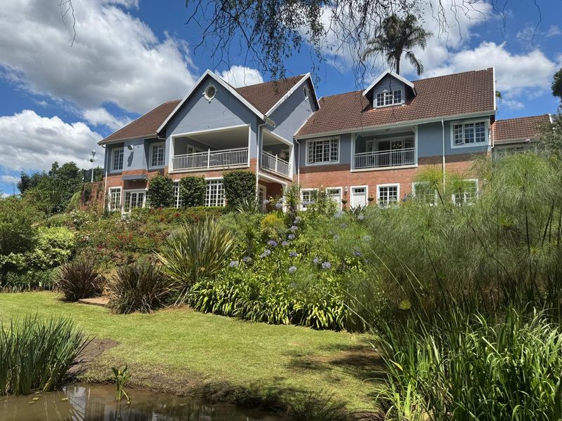 A spacious multi-story residence featuring a brick and painted facade, multiple balconies, and a beautifully landscaped garden with a pond.