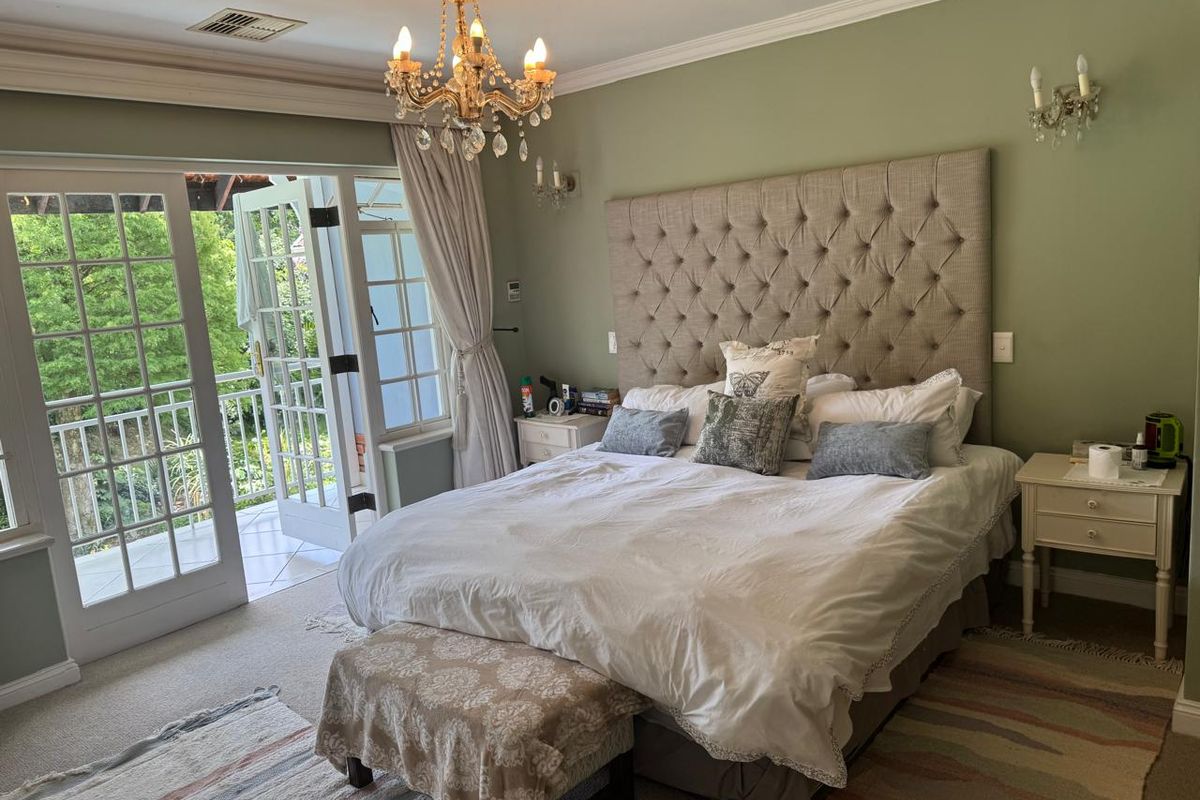 A spacious bedroom featuring a tufted headboard, elegant chandelier, and direct access to a private balcony through classic french doors.
