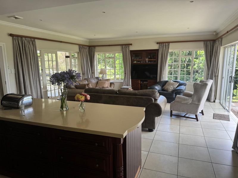 Spacious open-plan living area featuring a kitchen island, tiled flooring, and abundant natural light through multiple sets of french and sliding glass doors.
