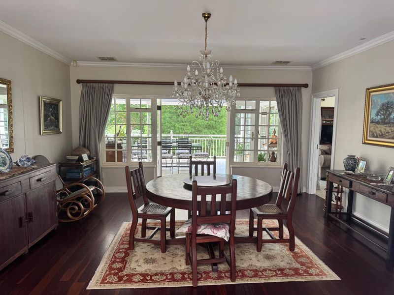 Elegant dining room featuring dark hardwood floors, a classic crystal chandelier, and large French doors providing natural light and access to the outdoor patio.