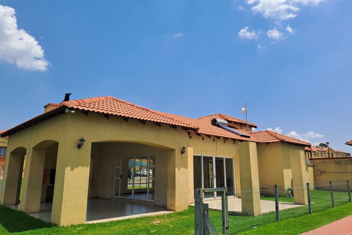 Rear view of a townhouse featuring a covered patio, terracotta tiled roof, solar water heating system, and a private fenced garden area.