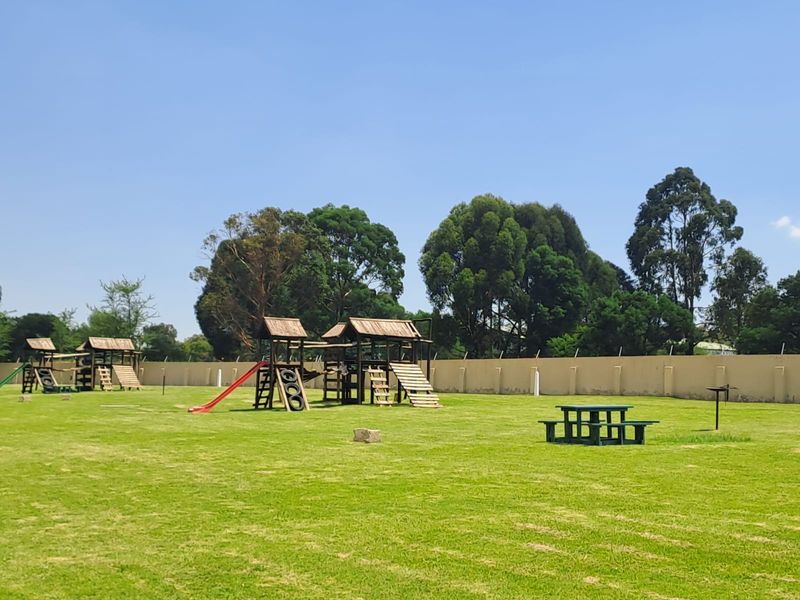 A spacious communal garden area featuring a well-maintained lawn and fixed wooden playground structures enclosed by a perimeter wall.