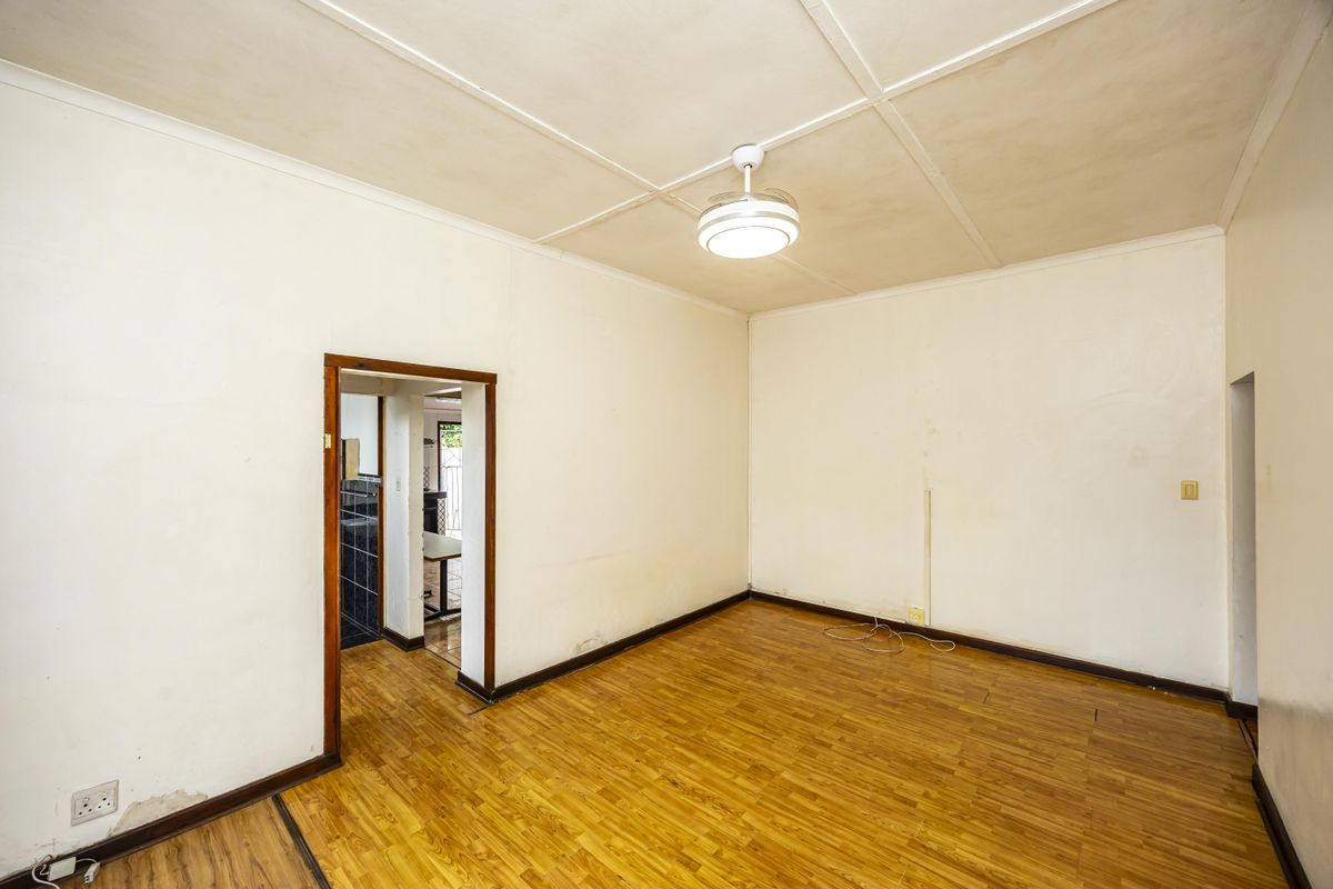 An empty living room featuring parquet flooring, a ceiling fan, and a doorway leading to an adjacent tiled area.