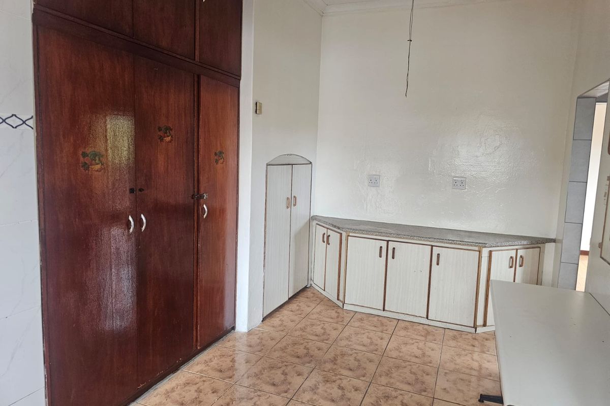 A functional kitchen area featuring built-in wooden cabinetry, stone-look countertops, and tiled flooring, offering potential for modernization and cosmetic updates.