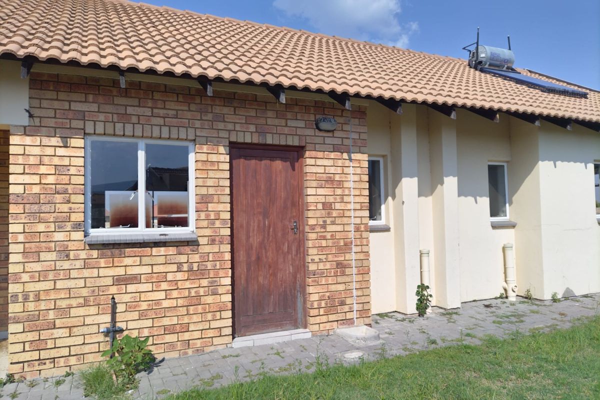 Rear exterior view of the house featuring face brick and plastered walls, a tiled roof, solar water heating system, and a paved walkway.
